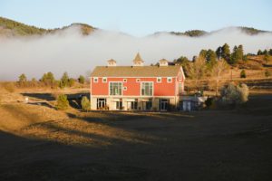 A red barn in the morning light sits against foggy mountains