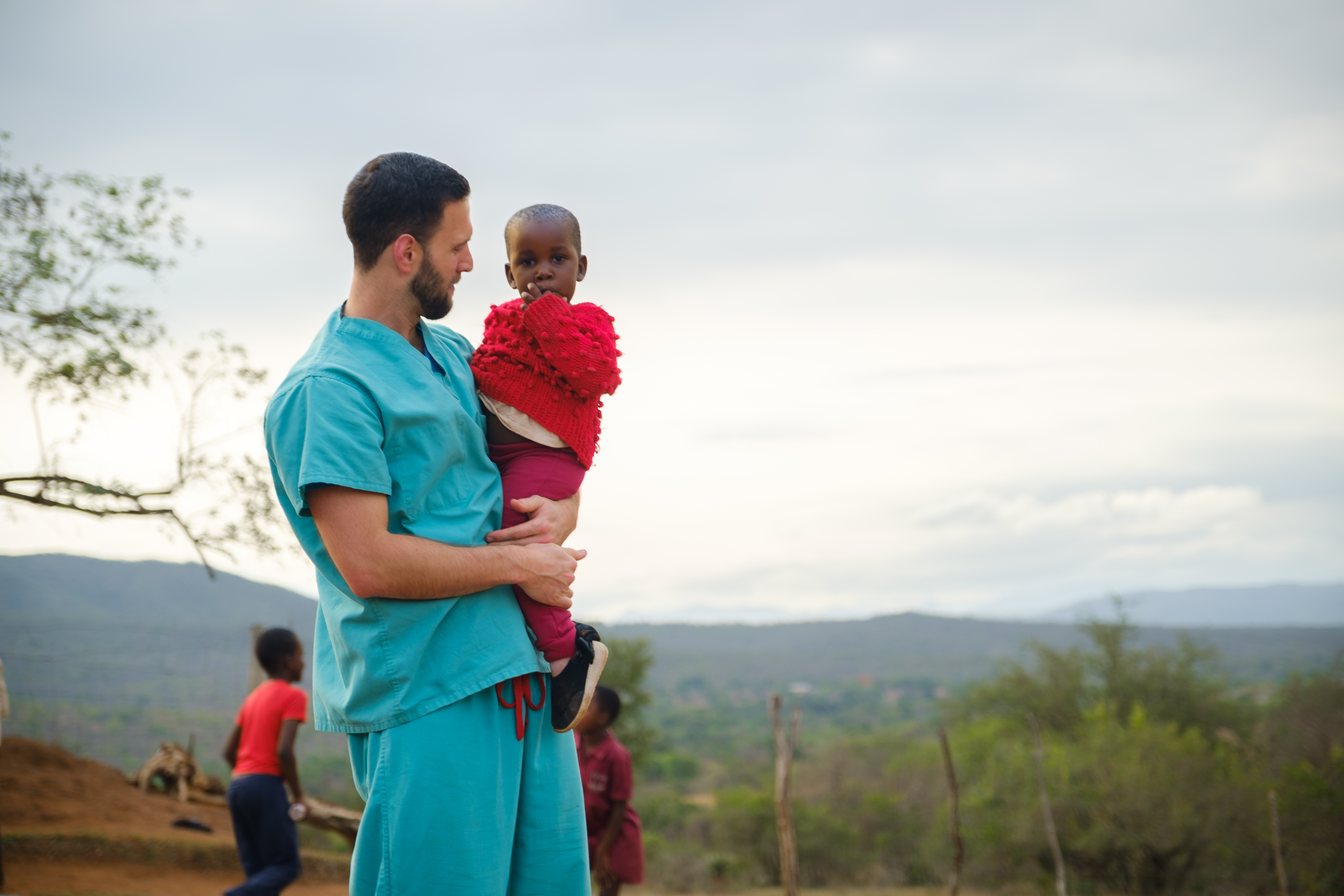 A man wearing medical scrubs holds a child in Eswatini