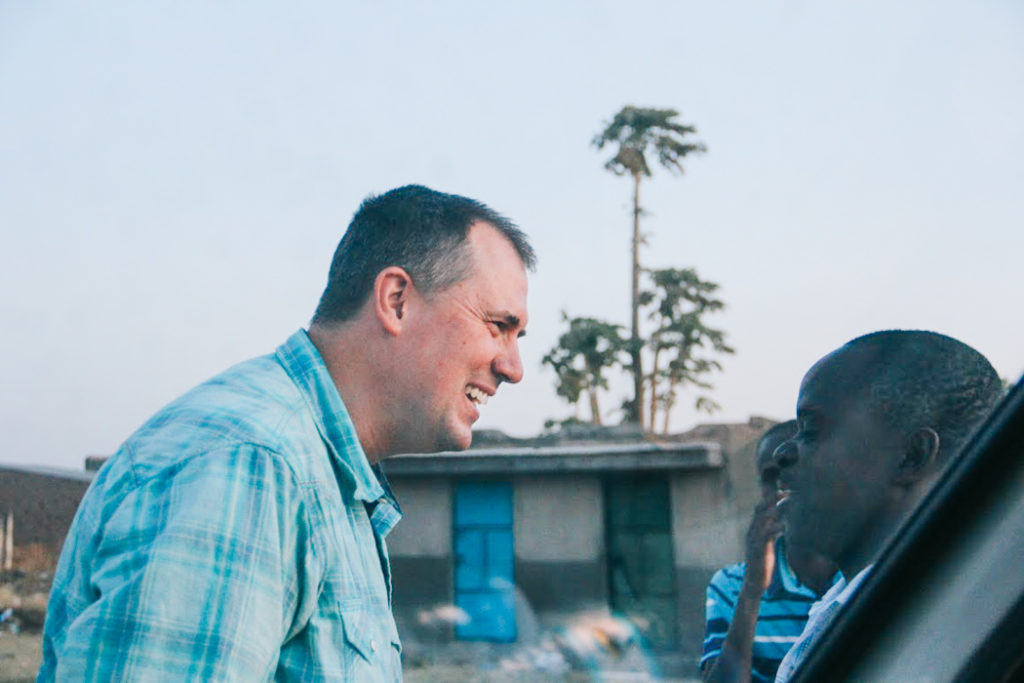 Wil in Uganda smiling and speaking with a teenage boy
