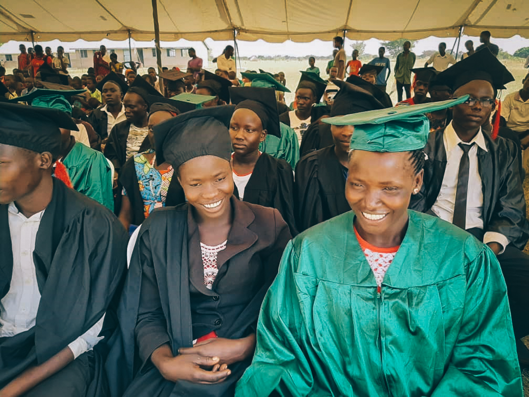 Two young Ugandan women in caps and gowns waiting to graduate