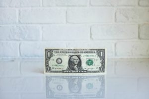 Single dollar standing upright against a white wall