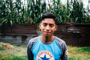 A Guatemalan teenager stands in front of a corn field