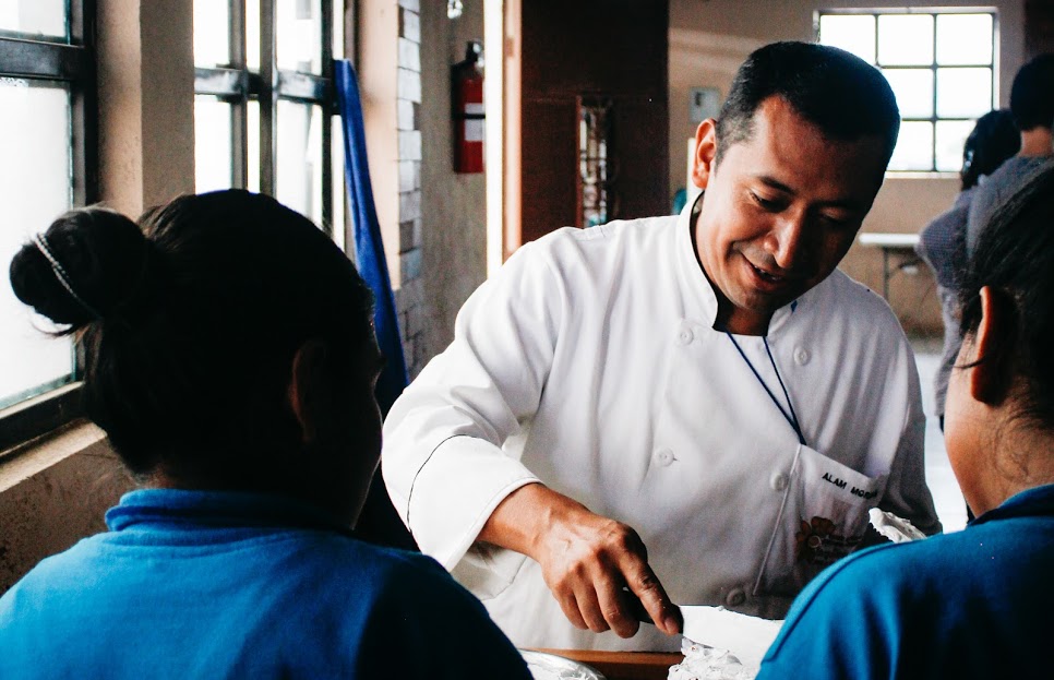 A Guatemalan man in a chef's coat ices a cake