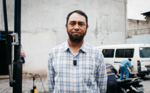 A Guatemalan man in a checkered shirt stands in front of a wall