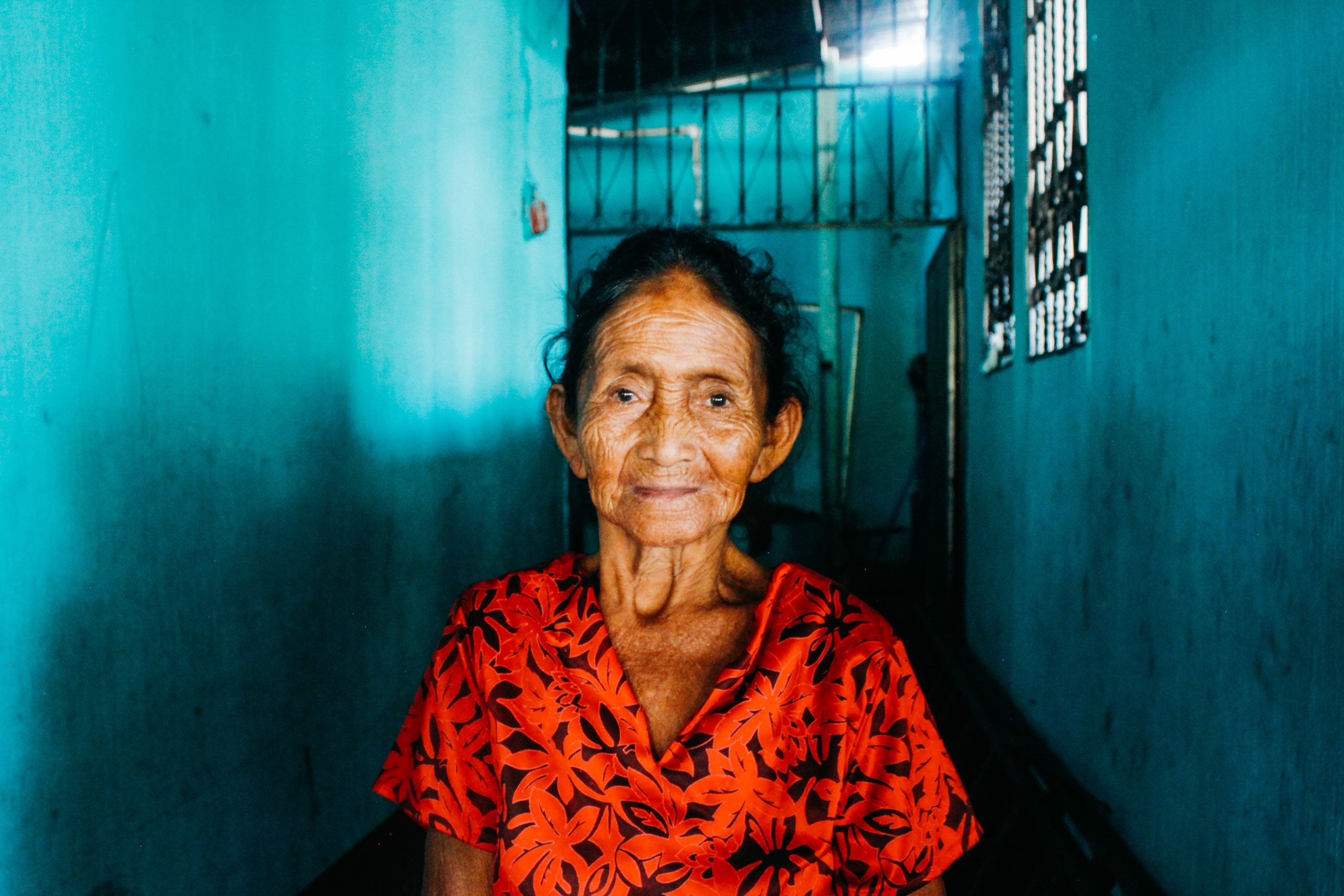 An older Guatemalan woman wearing red stands in a bright blue hallway