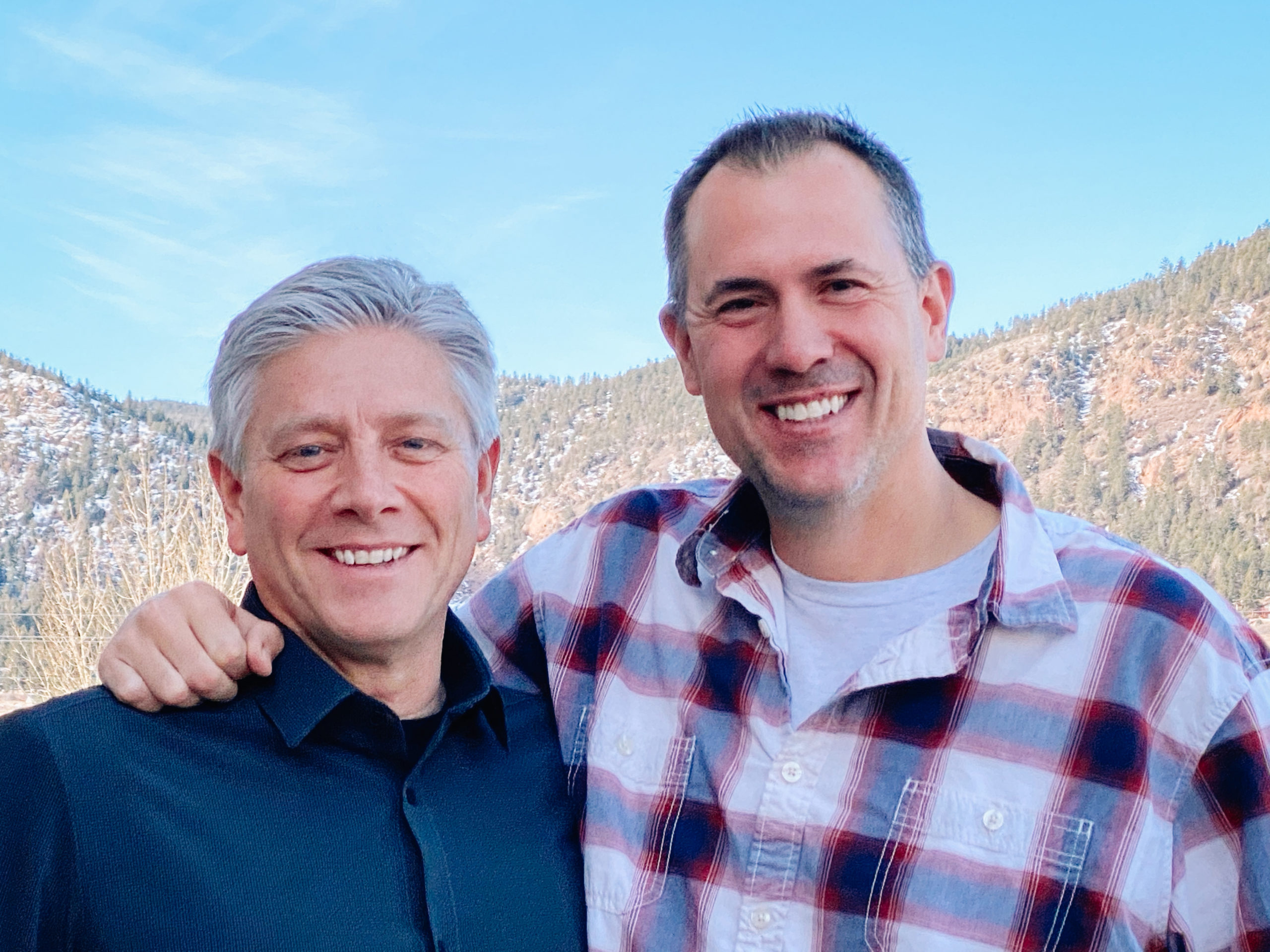 Ken and Wil smiling and embracing in front of the mountains in Colorado