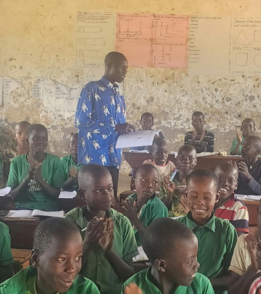 A photo of Michael wearing a blue shirt, standing among and instructing his students in Uganda.